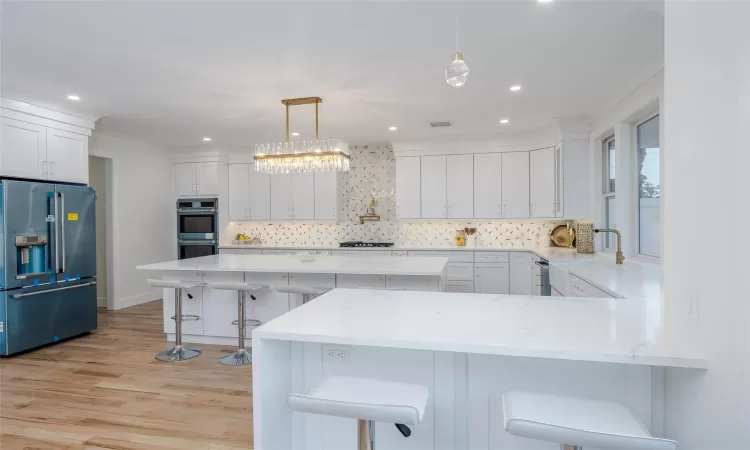 Kitchen with stainless steel appliances, pendant lighting, white cabinets, and a kitchen bar