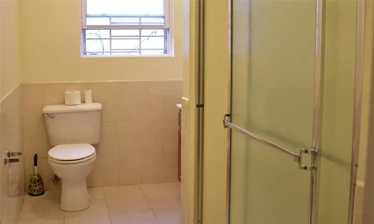 Bathroom with toilet, tile patterned floors, tile walls, and a shower with shower door