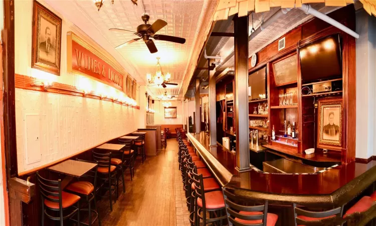 Bar with ceiling fan with notable chandelier, dark hardwood / wood-style flooring, and ornamental molding