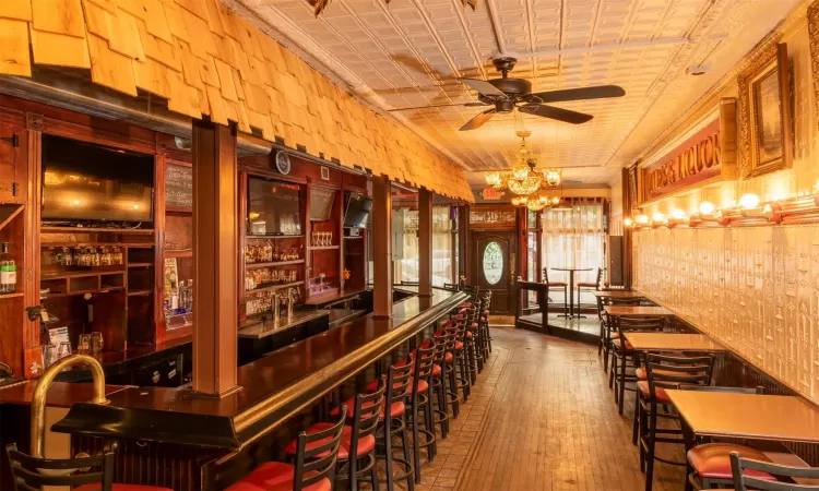 Bar with ceiling fan with notable chandelier and hardwood / wood-style floors