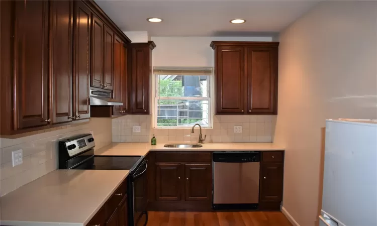 Kitchen with sink, dark hardwood / wood-style flooring, stainless steel appliances, and tasteful backsplash