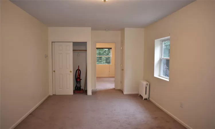 Unfurnished bedroom featuring light colored carpet, radiator heating unit, and a closet