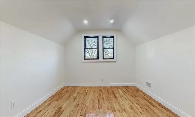 Additional living space with light hardwood / wood-style floors and vaulted ceiling