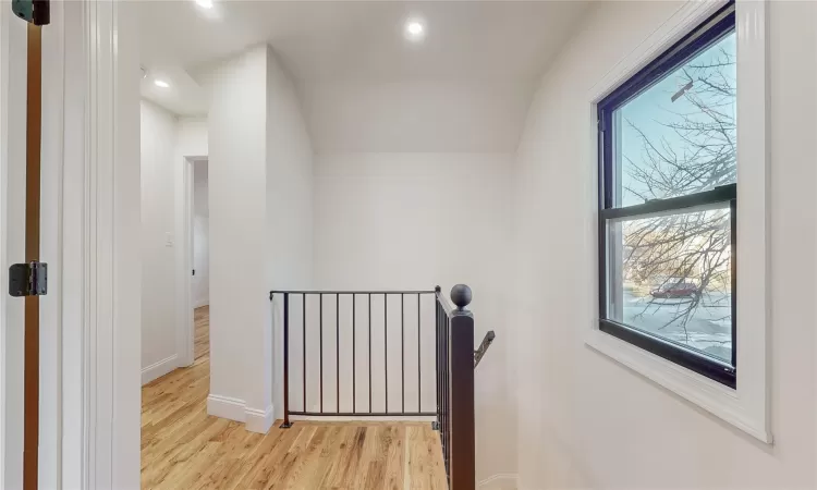 Corridor with a wealth of natural light, lofted ceiling, and light wood-type flooring