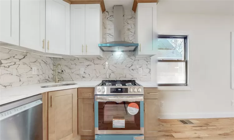 Kitchen featuring tasteful backsplash, stainless steel appliances, sink, wall chimney range hood, and white cabinetry