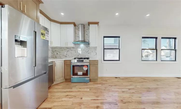 Kitchen with light wood-type flooring, stainless steel appliances, a wealth of natural light, and wall chimney exhaust hood