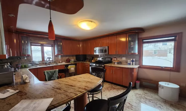 Kitchen featuring kitchen peninsula, a breakfast bar area, appliances with stainless steel finishes, tasteful backsplash, and pendant lighting