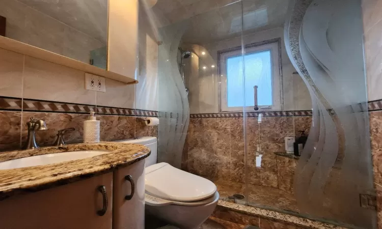 Bathroom featuring toilet, decorative backsplash, tile walls, an enclosed shower, and vanity