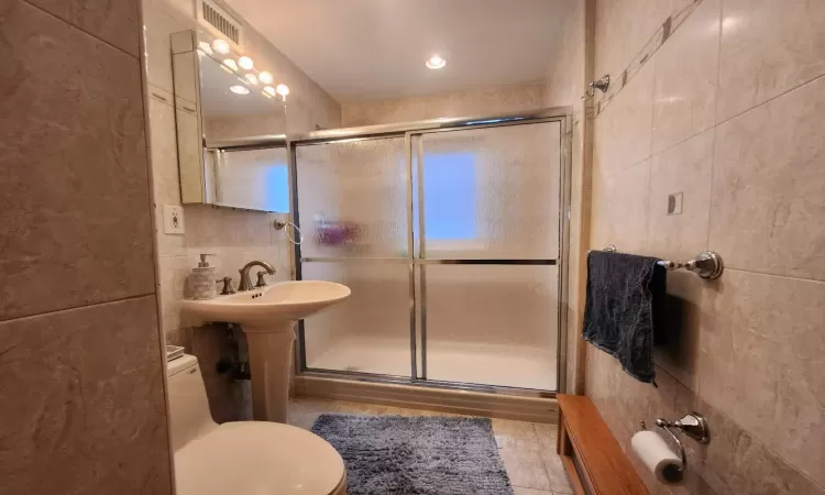 Bathroom featuring an enclosed shower, tile walls, tile patterned floors, and toilet