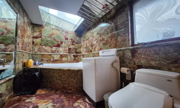 Bathroom featuring toilet, lofted ceiling, a bathtub, and washer / clothes dryer