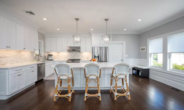 Kitchen with white cabinets, a kitchen island, stainless steel appliances, and pendant lighting