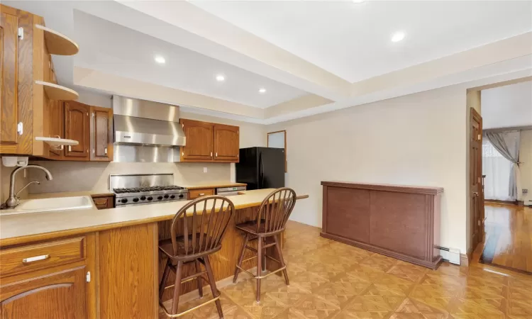 Kitchen with a breakfast bar, sink, black refrigerator, ventilation hood, and range