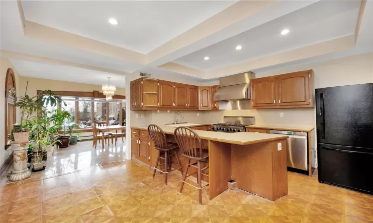 Kitchen with black fridge, stainless steel dishwasher, a breakfast bar, wall chimney exhaust hood, and range