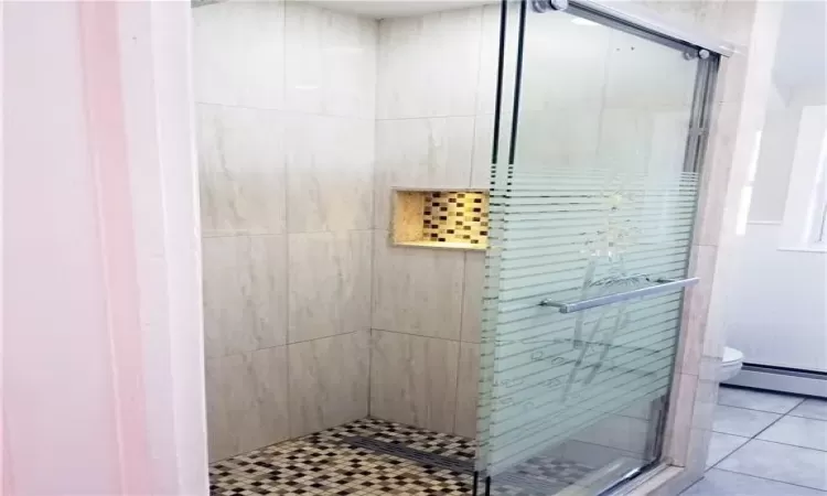 Bathroom featuring a shower with shower door, a baseboard heating unit, tile patterned floors, and toilet