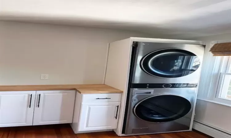 Washroom featuring cabinets, baseboard heating, dark hardwood / wood-style flooring, and stacked washer and clothes dryer