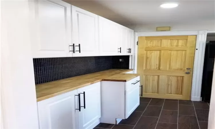 Kitchen featuring butcher block countertops, white cabinets, and tasteful backsplash