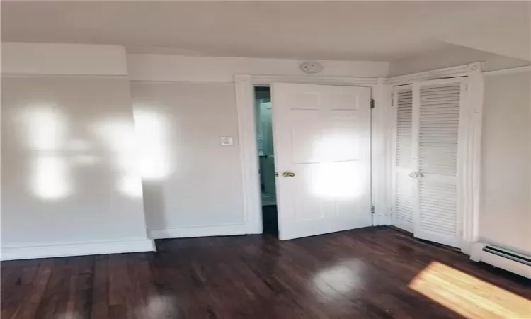 Bedroom bedroom with baseboard heating, a closet, and dark hardwood / wood-style floors