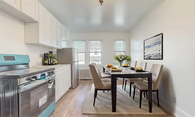 Kitchen featuring white cabinetry, appliances with stainless steel finishes, light wood-type flooring, crown molding, and radiator heating unit