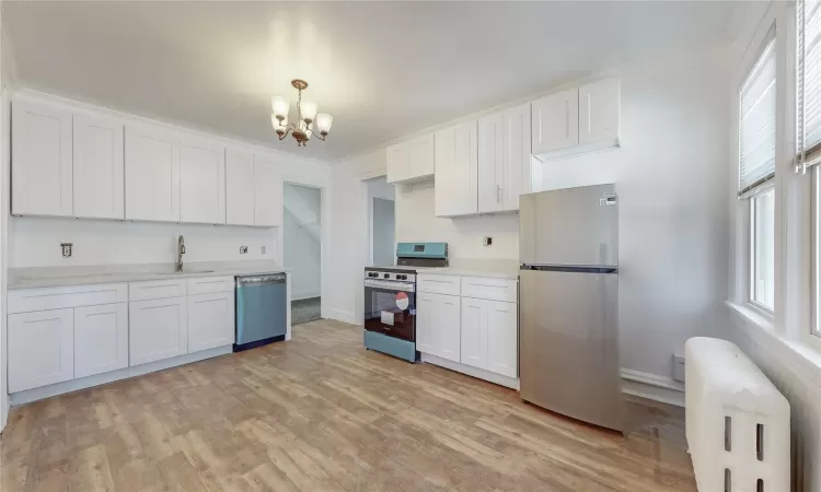 Kitchen with an inviting chandelier, white cabinetry, appliances with stainless steel finishes, radiator, and sink