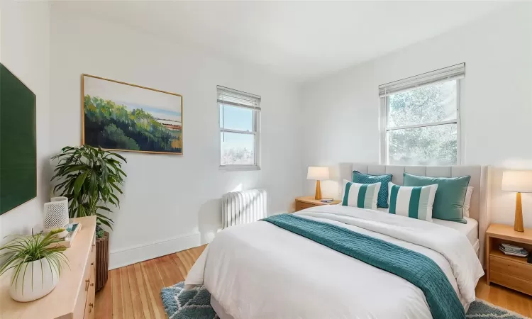 Bedroom with light wood-type flooring, multiple windows, and radiator heating unit