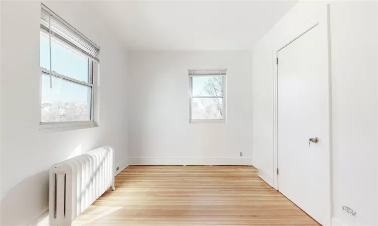 Unfurnished bedroom featuring light hardwood / wood-style floors, multiple windows, and radiator heating unit