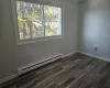 Unfurnished room featuring a baseboard heating unit and dark hardwood / wood-style floors