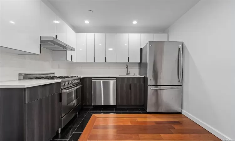 Kitchen with dark hardwood / wood-style floors, wall chimney range hood, sink, white cabinetry, and stainless steel appliances