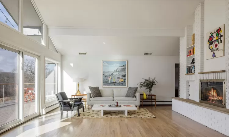 Living room with a fireplace, wood-type flooring, a baseboard heating unit, and vaulted ceiling