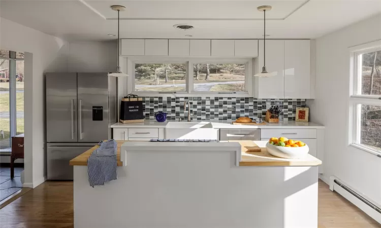 Kitchen featuring appliances with stainless steel finishes, pendant lighting, white cabinetry, and a baseboard radiator