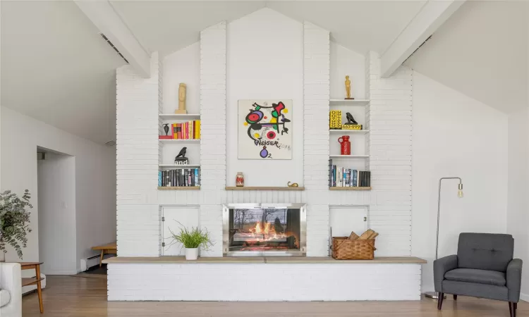 Living room with a fireplace, baseboard heating, built in features, and vaulted ceiling with beams