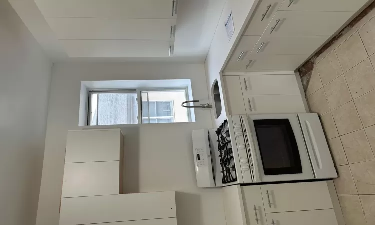 Kitchen with sink, white cabinetry, and stove