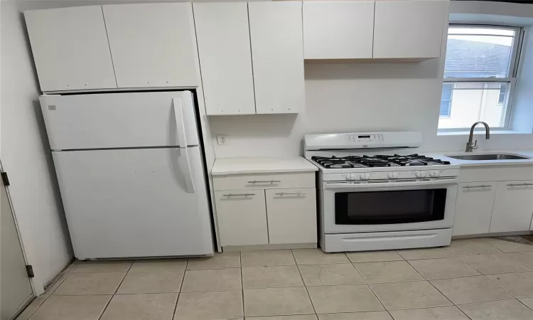 Kitchen featuring sink, white appliances, white cabinets, and light tile patterned flooring