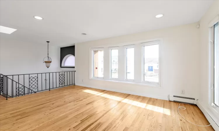 Spare room featuring a healthy amount of sunlight, a skylight, baseboard heating, and light hardwood / wood-style flooring