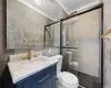 Bathroom with tile walls, an enclosed shower, vanity, and toilet