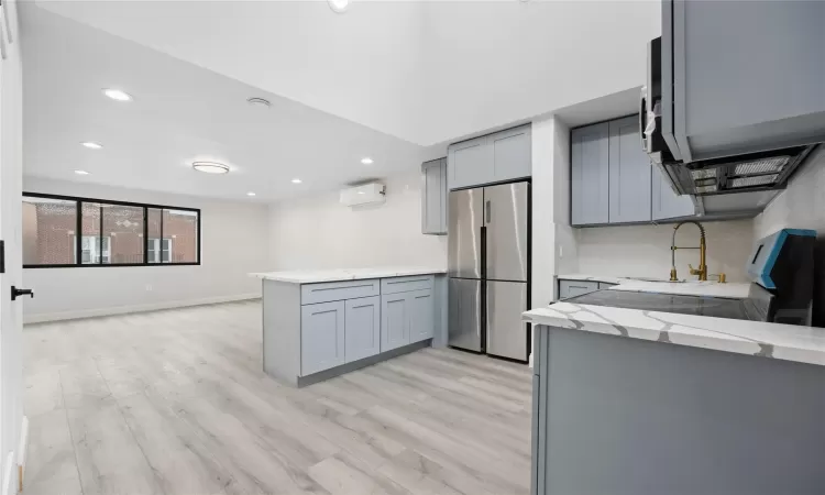 Kitchen with a wall unit AC, kitchen peninsula, sink, gray cabinetry, and stainless steel fridge