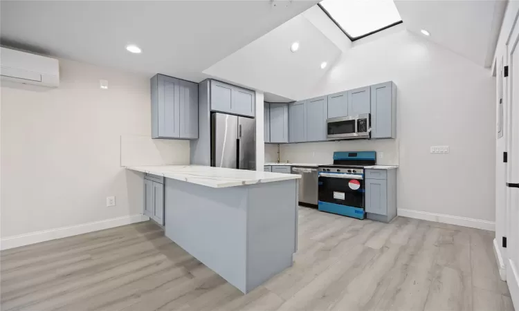 Kitchen with kitchen peninsula, a wall unit AC, stainless steel appliances, light wood-type flooring, and high vaulted ceiling