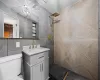 Bathroom with toilet, vanity, tile walls, and tiled shower