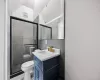 Bathroom featuring a shower with door, vanity, tasteful backsplash, tile walls, and toilet