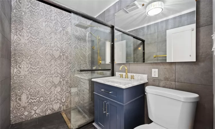 Bathroom featuring toilet, a shower, tile walls, and vanity