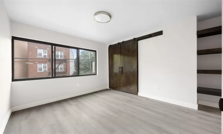 Unfurnished bedroom featuring light hardwood / wood-style floors and a barn door