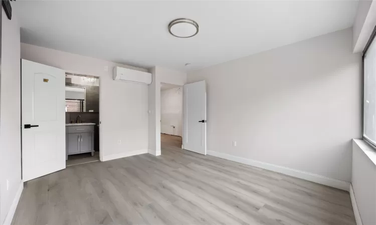 Unfurnished bedroom featuring ensuite bath, light wood-type flooring, and a wall unit AC