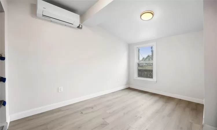 Unfurnished room with lofted ceiling with beams, a wall unit AC, and light wood-type flooring