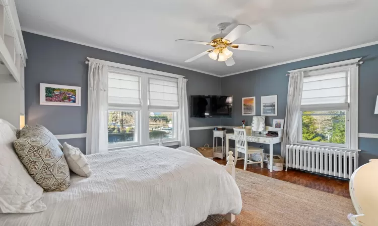 Bedroom featuring ceiling fan, dark wood-type flooring, multiple windows, and radiator heating unit