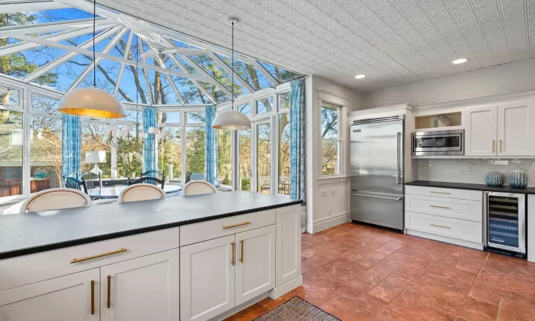 Kitchen with decorative light fixtures, white cabinetry, built in appliances, wine cooler, and decorative backsplash