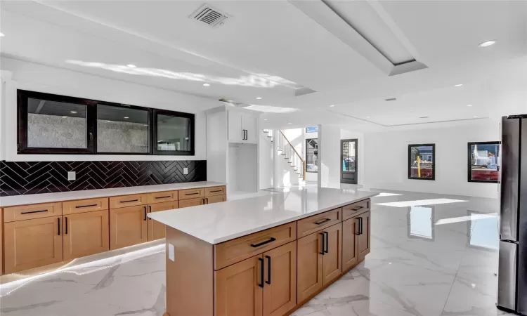 Kitchen featuring a spacious island, white cabinets, stainless steel fridge, and tasteful backsplash