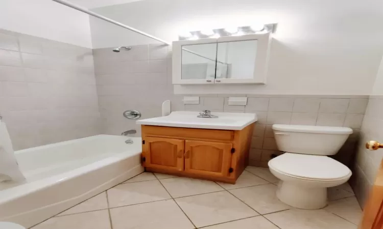 Full bathroom with tiled shower / bath, tile patterned flooring, vanity, tile walls, and toilet