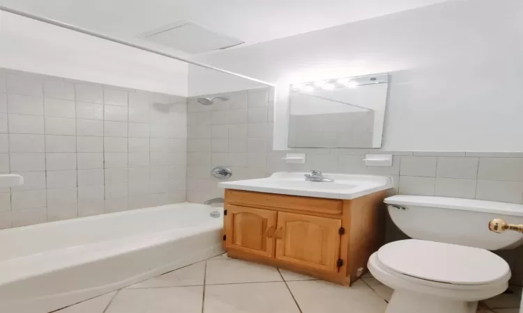 Full bathroom with tiled shower / bath combo, tile patterned floors, vanity, tile walls, and toilet