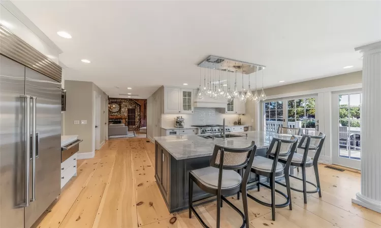 Kitchen with a large island with sink, hanging light fixtures, light stone countertops, white cabinetry, and stainless steel built in refrigerator