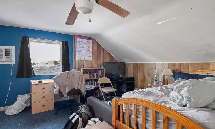 Bedroom with wooden walls, vaulted ceiling, ceiling fan, carpet floors, and a wall mounted air conditioner