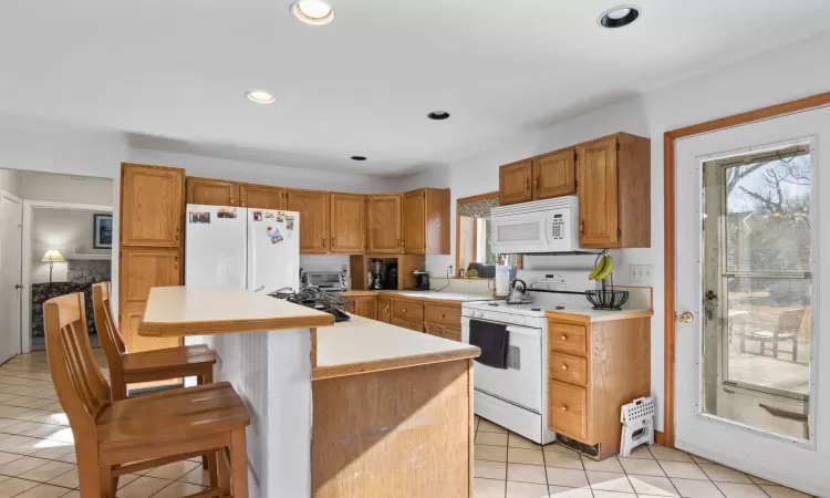 Kitchen with white appliances, a kitchen breakfast bar, light tile patterned floors, a kitchen island, and sink